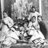 Studio portrait typifying a contemporaneous Occidental view of China, including opium smoking and young 'singsong' girls with bound feet. Dated to the end of the Qing era, probably c. 1900.